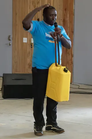 Father Joseph explaining how women carry the heavy water jugs. Photo by Patrick Hurley