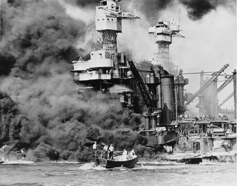 Pearl Harbor, Hawaii. A small boat rescues a seaman from the 31,800 ton USS West Virginia burning in the foreground. Smoke rolling out amidships shows where the most extensive damage occurred. Note the two men in the superstructure. The USS Tennessee is inboard