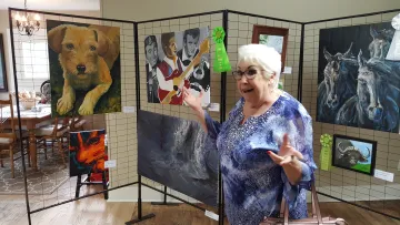 Woman looks surprised in front of painting with a large ribbon that says Best Heritage