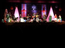Stage decorated with trees and presents for Christmas with a band of musicians on stage